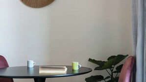 A round table with a book and two mugs, a large plant, and a wall with a circular mirror.