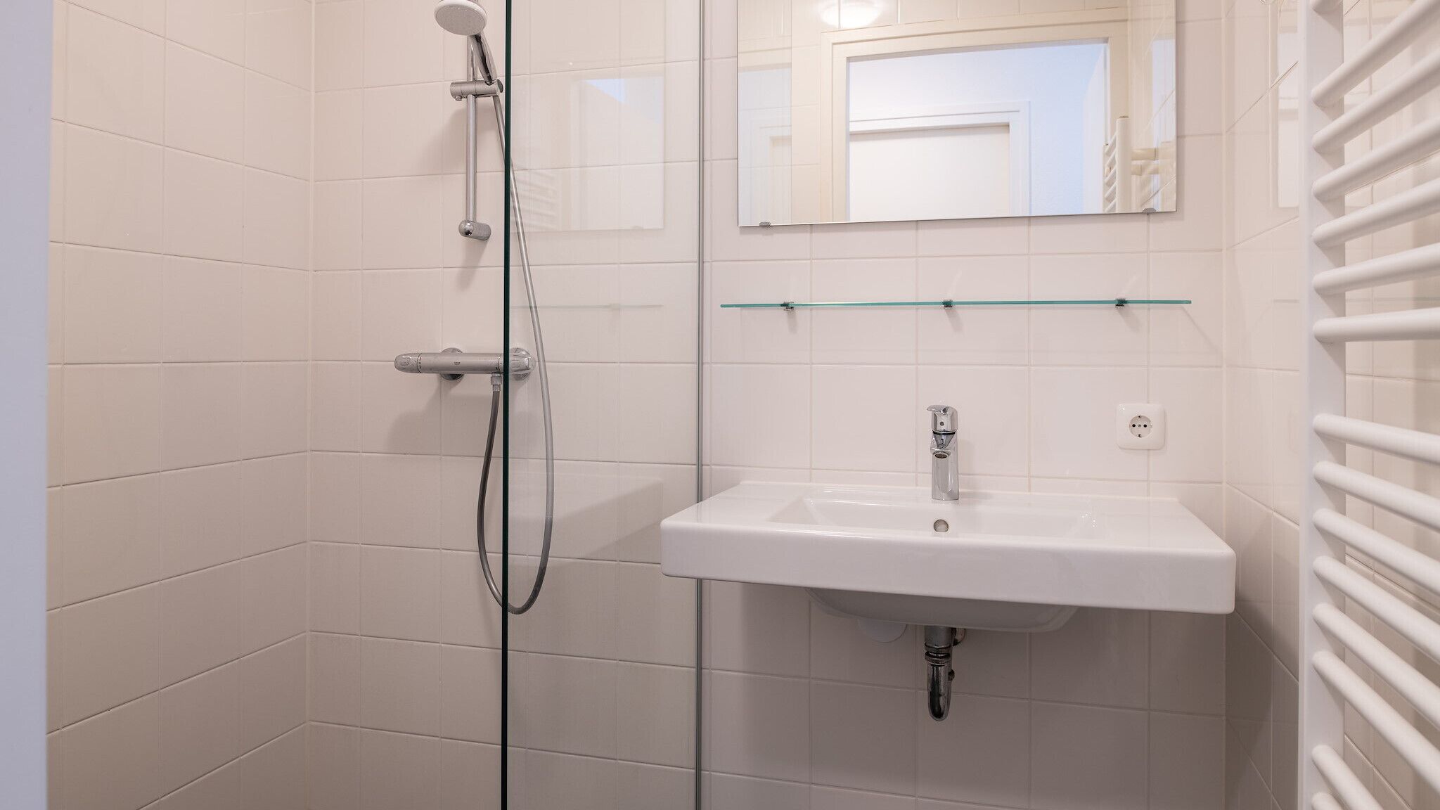Een badkamer met een douchecabine van glas, een wit wastafelmeubel en een spiegel erboven.