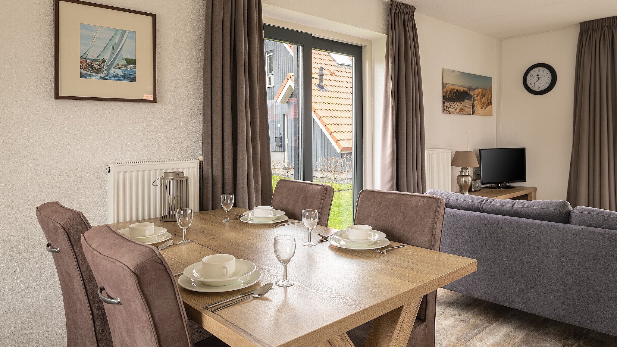 A dining area with a table set for four, a sofa, a television, and a clock on the wall.