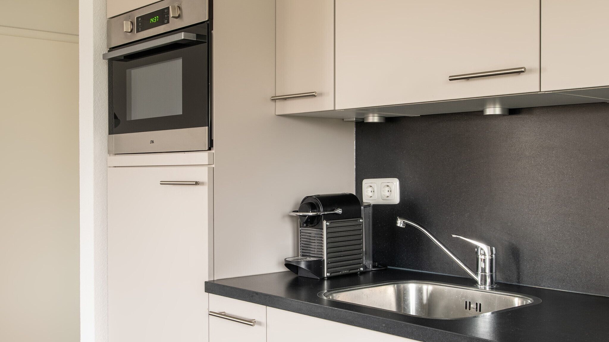 A modern kitchen with a built-in oven, a stainless steel sink, and a black countertop.
