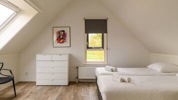 Ein Schlafzimmer mit schrägen Wänden, einem Heizkörper, einem Bett mit weißer Bettwäsche, einer weißen Kommode und einem gerahmten Bild an der Wand.