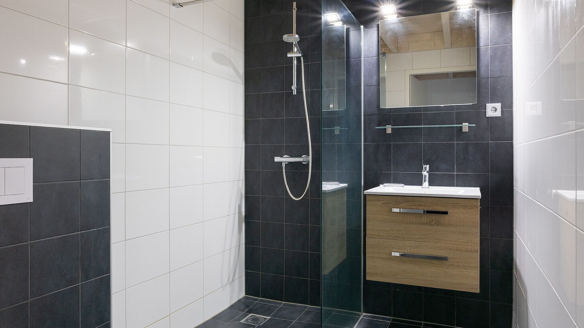 Un bagno moderno con cabina doccia in vetro, mobile bagno in legno e uno specchio grande.