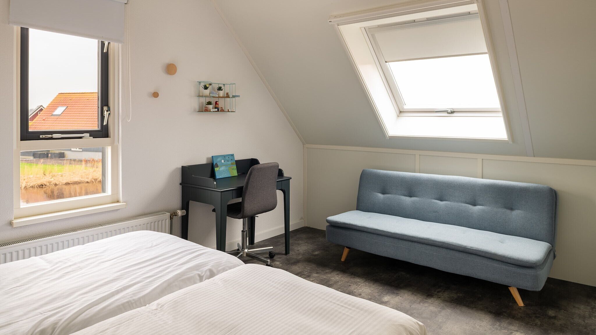 Un dormitorio con cama, escritorio, silla, sofá y dos ventanas.