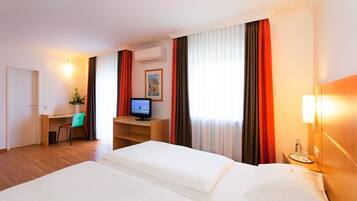 A hotel room with two beds, a desk, a chair, a television, and a window with curtains.