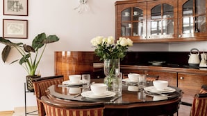 A dining area with a round table set for four, surrounded by chairs. There is a potted plant to the left and a cabinet with glass doors above the table. - Apartamenty Sun & Snow Sw. Tomasza (Kraków)