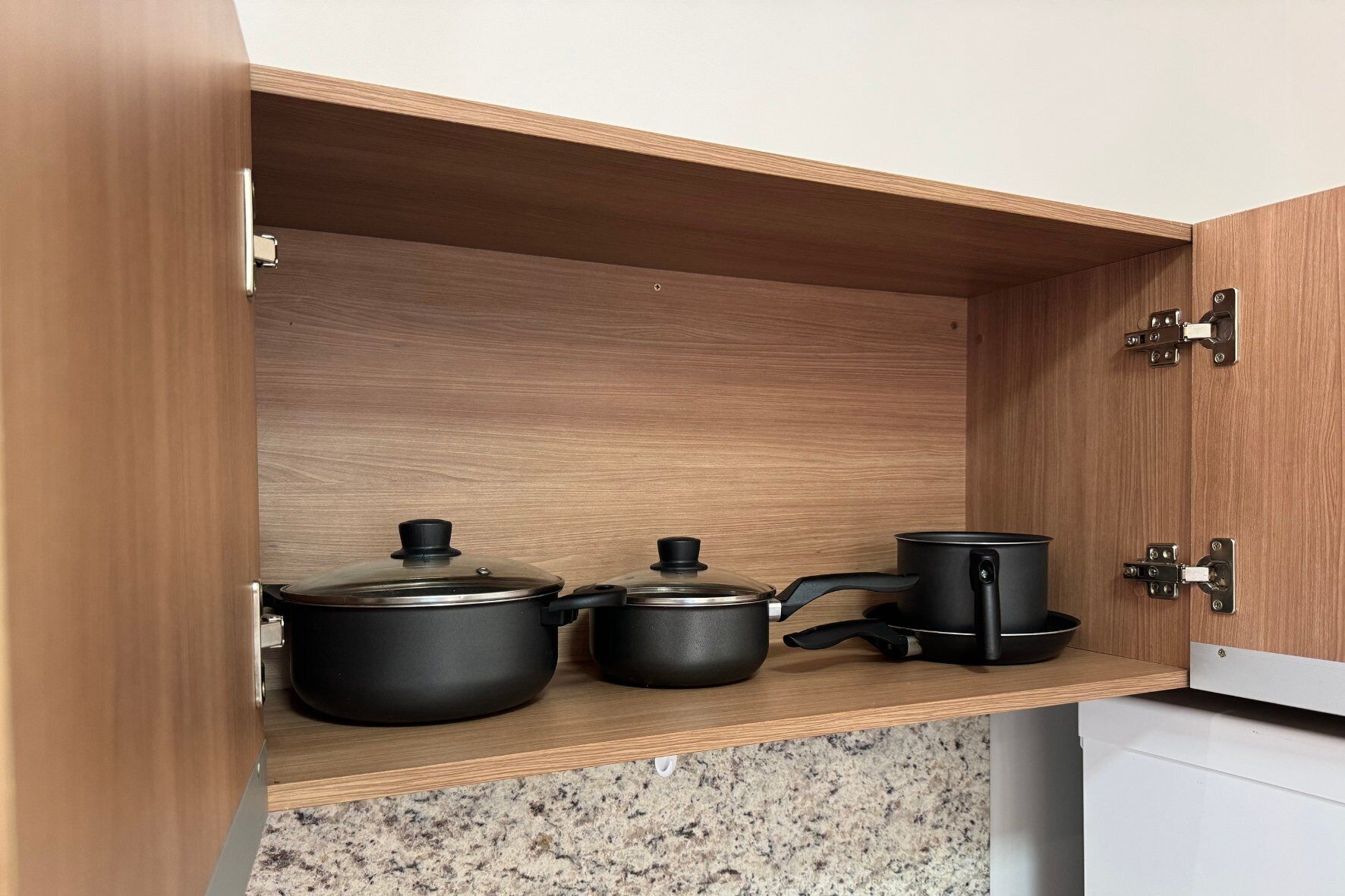 A kitchen cabinet with three black pots and pans.