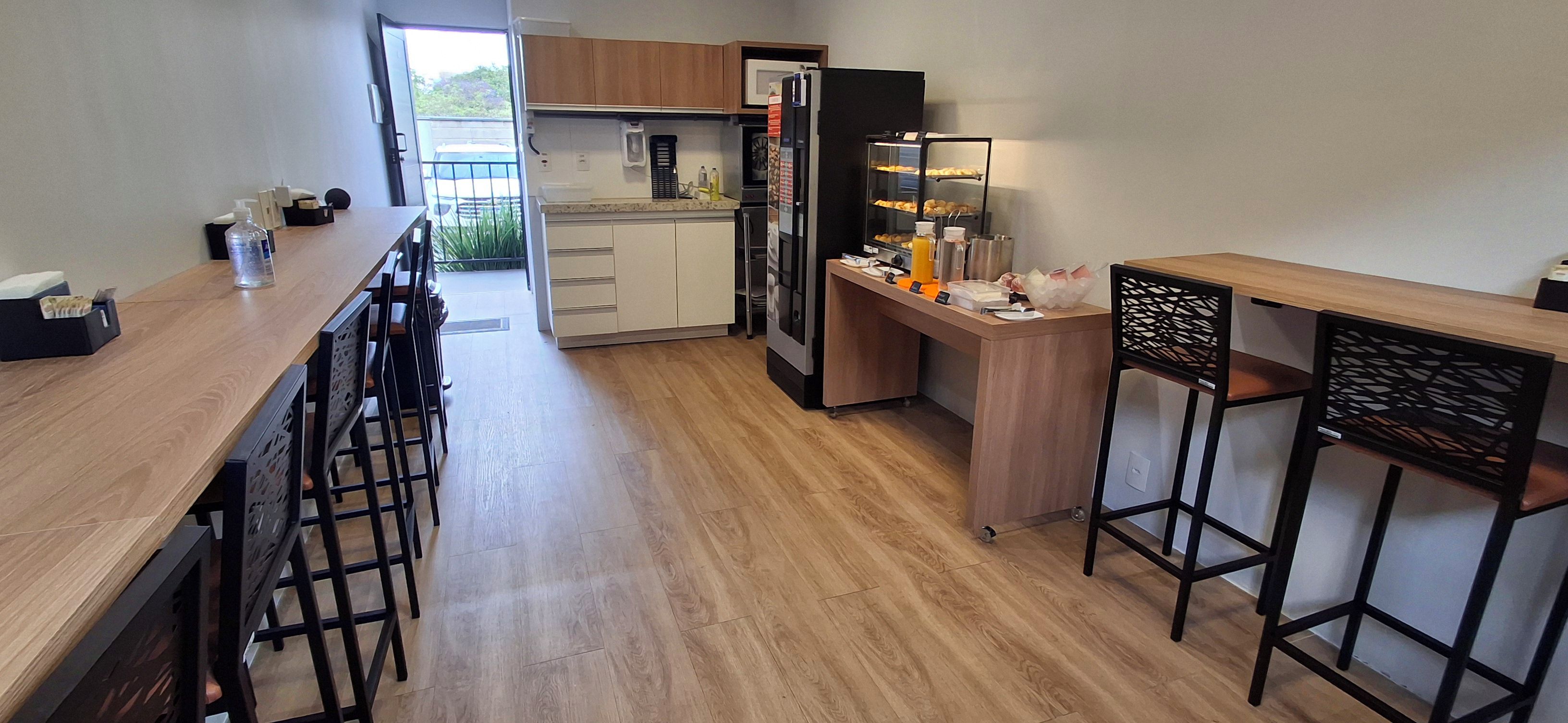 Cozinha moderna com bancadas de madeira, forno embutido e geladeira. Há banquetas de bar e um pequeno espaço para bar.
