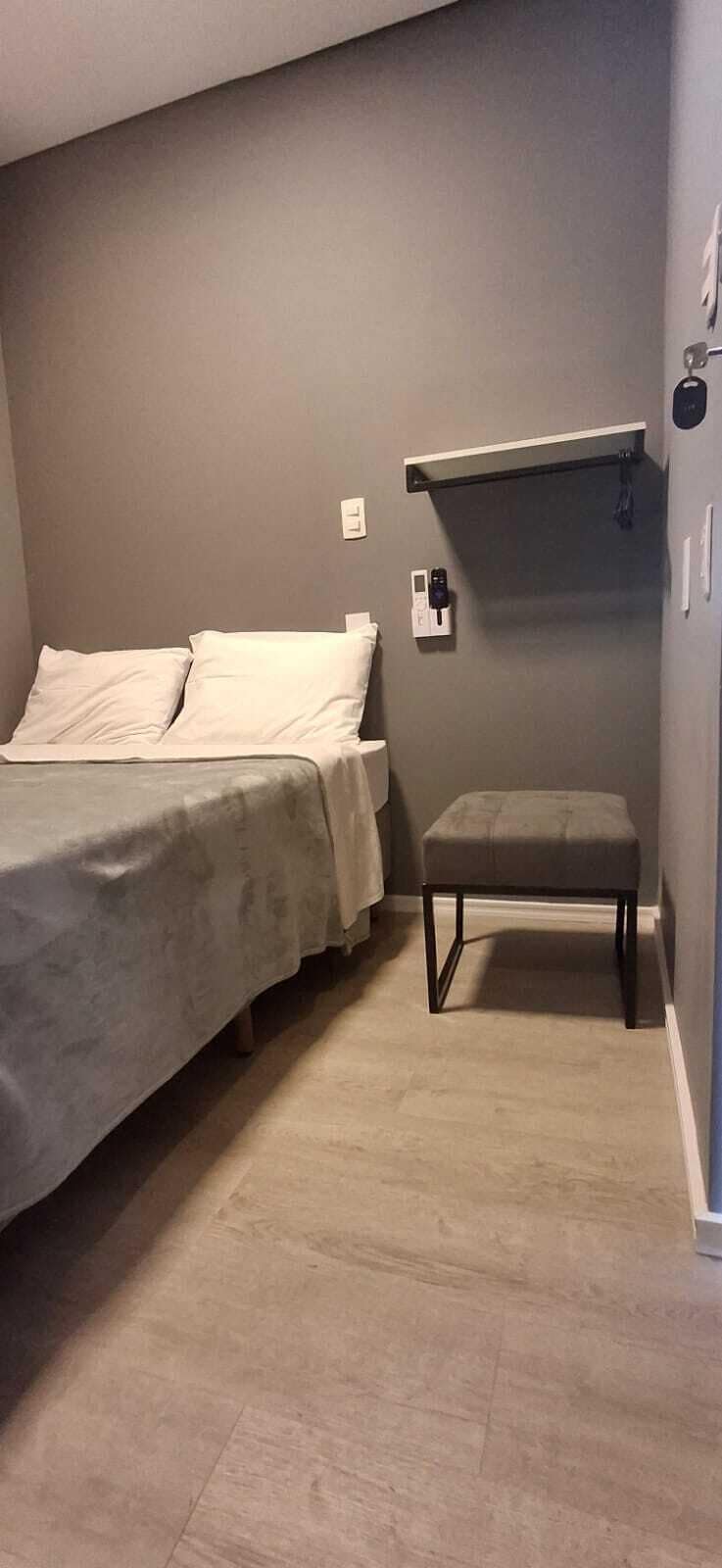 A bedroom with a bed, a bench, and a shelf against the wall.