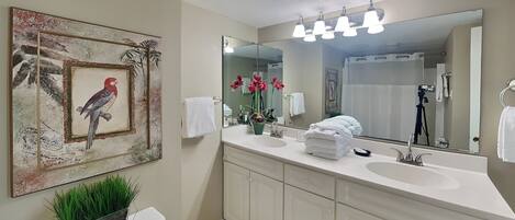 A bathroom with a large mirror, white cabinets, a toilet, and a framed picture of a bird.