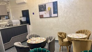 A lobby with a reception desk, a coffee machine, and seating areas with floral-patterned tables and chairs.