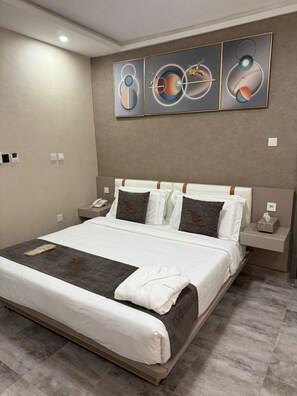 A modern hotel room with a large bed, bedside tables, and abstract wall art. - Hotel Millennium  (Nouadhibou)