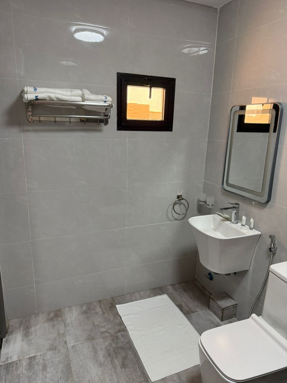 A bathroom with a white sink, a mirror, a towel rack, and a window.