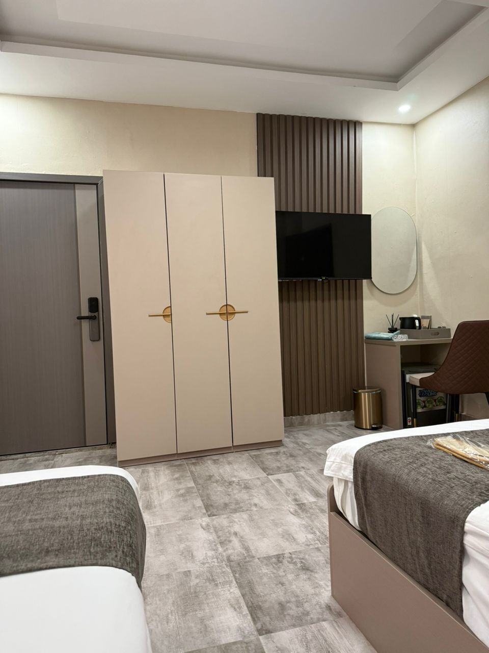 Quarto de hotel com guarda-roupa, secretária e cadeira, cama e televisão.