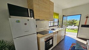 A compact kitchen with a refrigerator, oven, and microwave. There is a window providing a view of the outdoors.