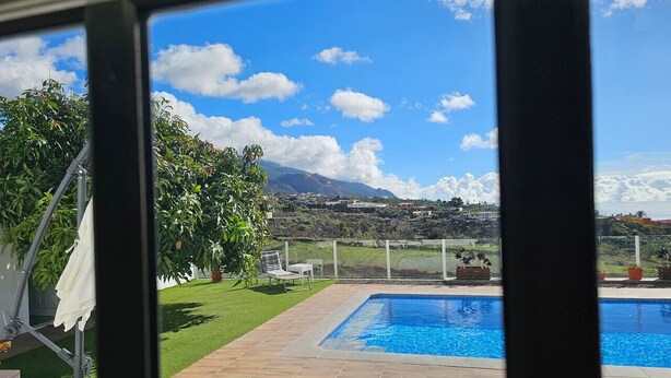 A pool area with a view of a mountain range, a lawn, and a few potted plants.