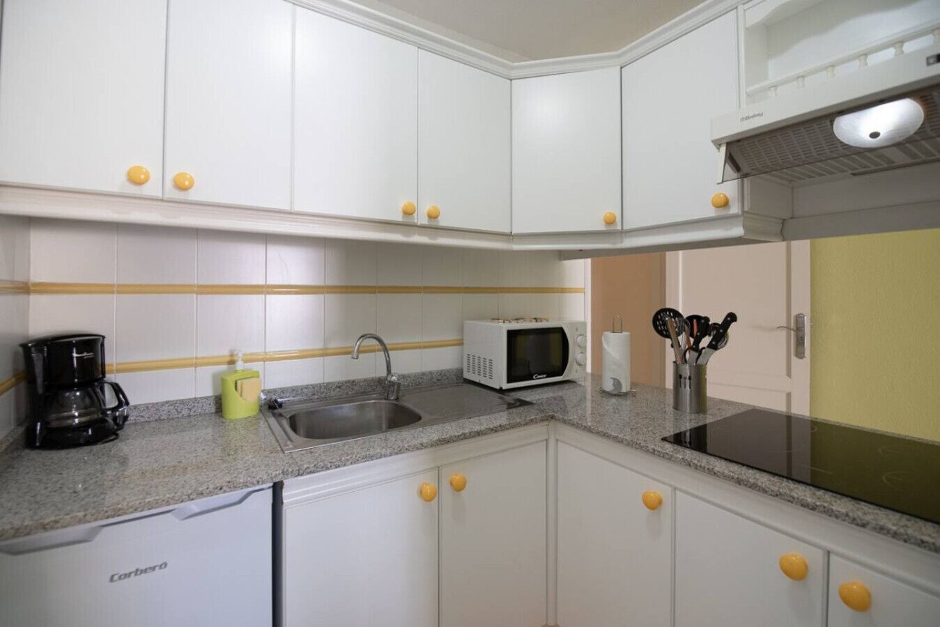 A compact kitchen with white cabinets, a granite countertop, a coffee maker, a microwave, and a sink.