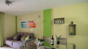 A living room with a sofa, dining table, chairs, a painting, a fan, and a shelf with decorative items. - Casa Angel - Puerto Naos (Puerto de Naos)