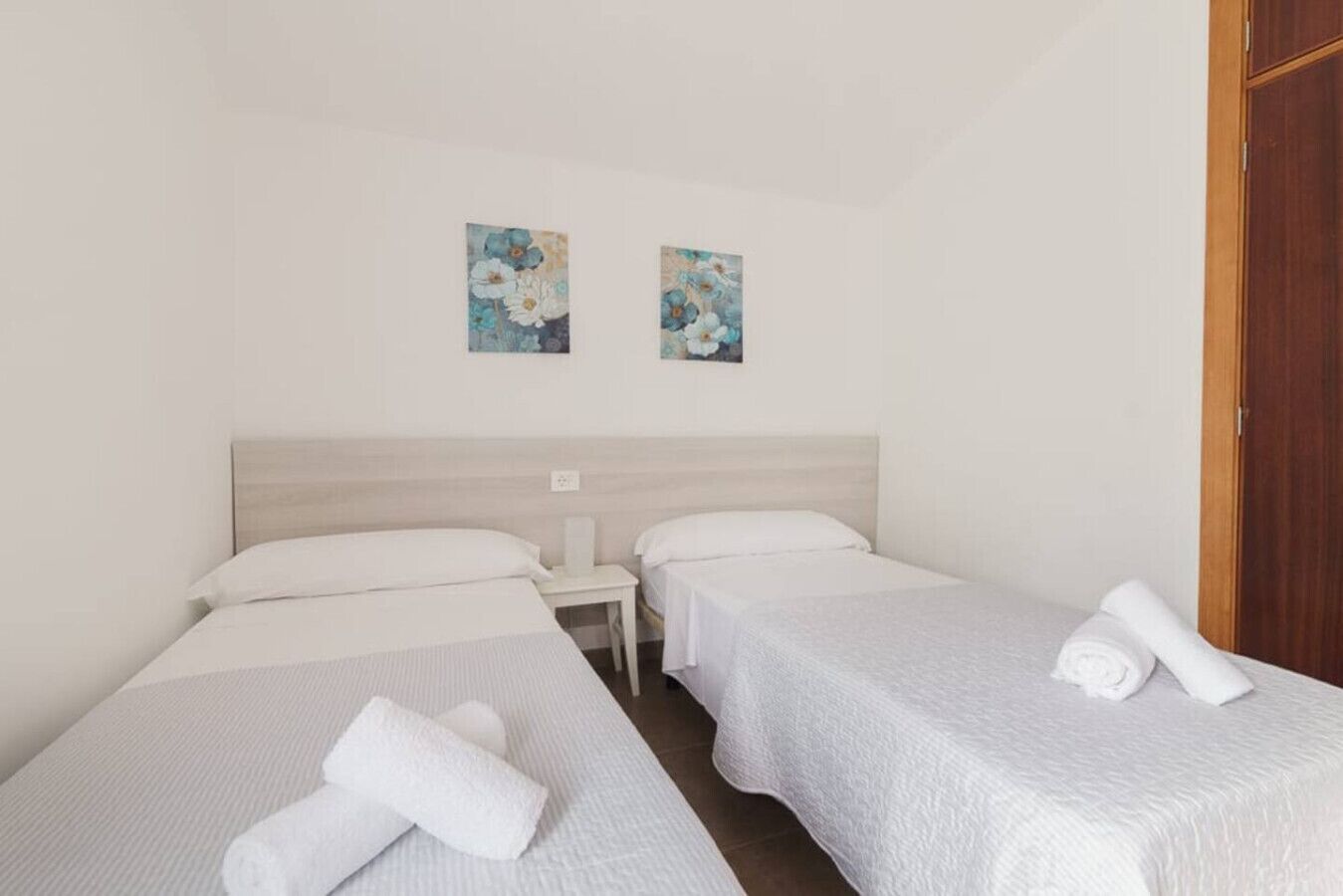 Ett hotellrum med två separata sängar, ett litet sängbord och två tavlor som hänger på väggen.