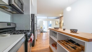 A modern kitchen with a gas stove, microwave, and wooden shelves. - XL Prime Tribeca Furnished Loft (New York)