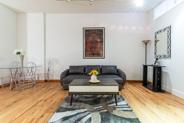 Ein modernes Wohnzimmer mit einem dunkelbraunen Ledersofa, einem Glastisch und einem gerahmten Kunstwerk an der Wand.