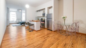 A modern kitchen with stainless steel appliances, a dining area with clear chairs, and a small island with bar stools. - XL Prime Tribeca Furnished Loft (New York)