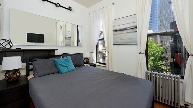 Un dormitorio con cama, televisión, espejo y ventana con cortinas.