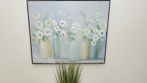 Una mesa redonda blanca con dos sillas grises, una planta en maceta y un cuadro de flores en la pared.