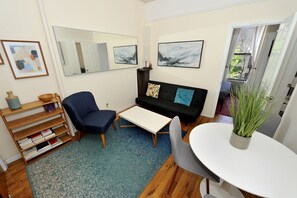 A modern living room with a sofa, a coffee table, a bookshelf, and a dining table. - 3BR Apartment in Big Apple (New York)