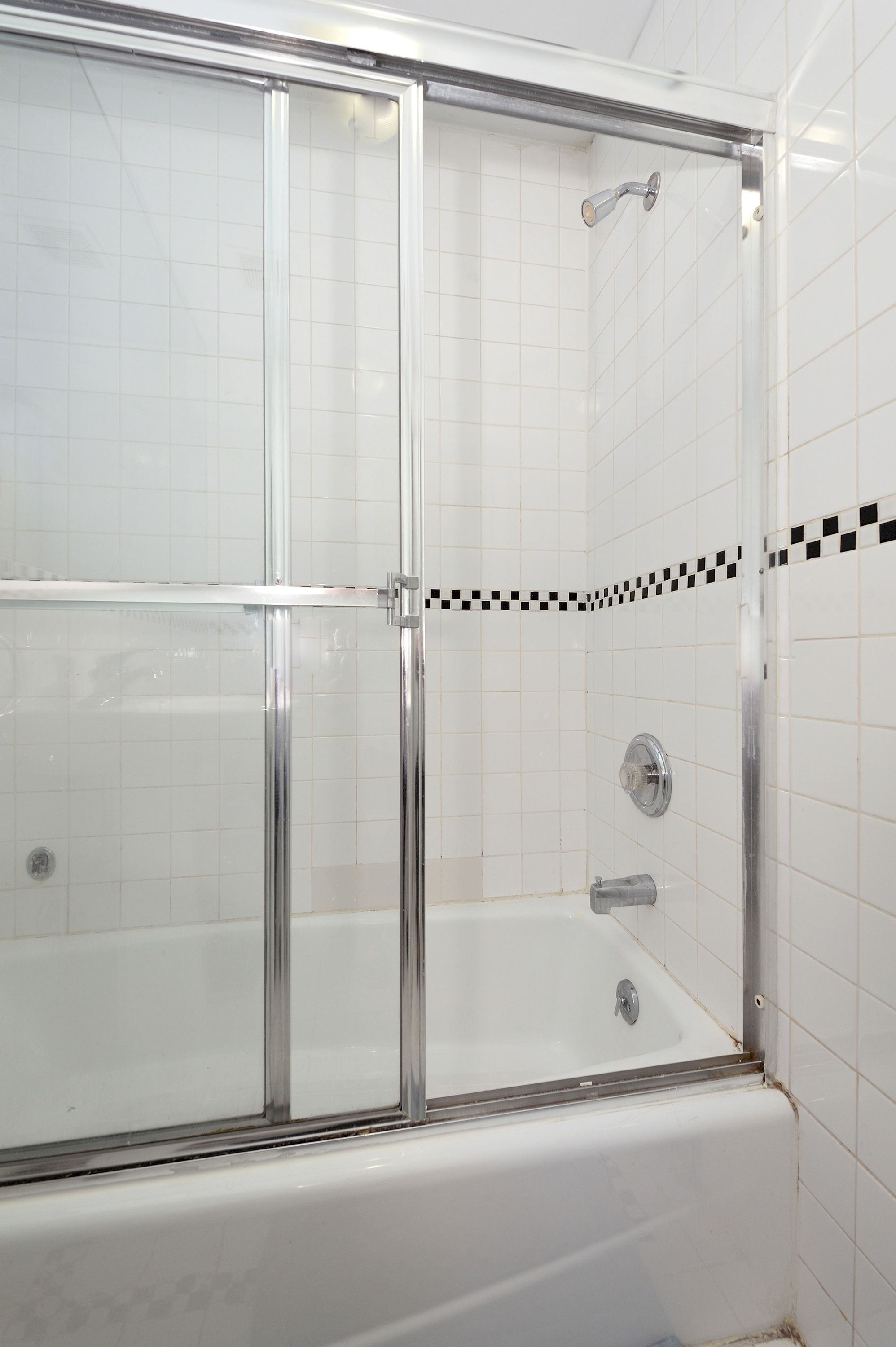 Ducha con cerramiento de vidrio, pared de azulejos blancos y un borde de baldosas a cuadros.