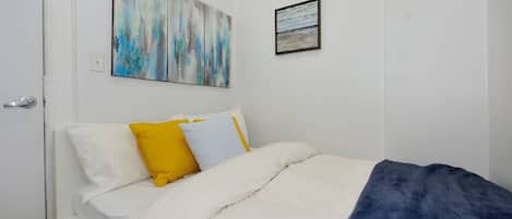 A bedroom with a bed, white walls, a door, and two paintings.