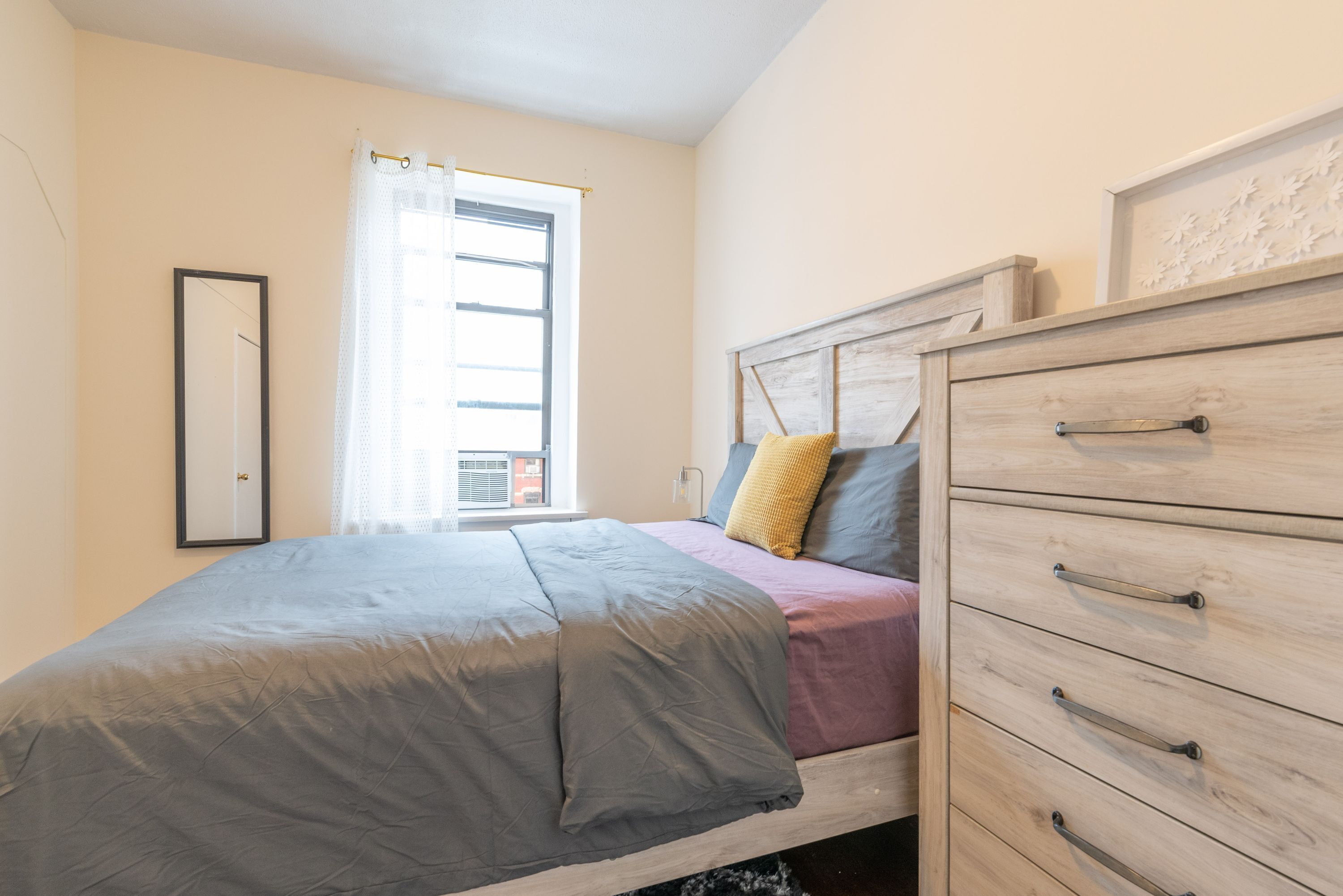 Un dormitorio con cama, cómoda, cortinas en la ventana y espejo.