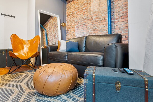 A modern living room with a leather sofa, a leather armchair, a patterned rug, a leather pouf, and a vintage suitcase. - Hudson Yards Prime Location Furnished Rental (New York)