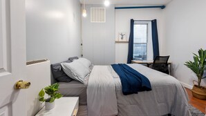 A modern bedroom with a bed, bedside table, potted plant, and a window with curtains.