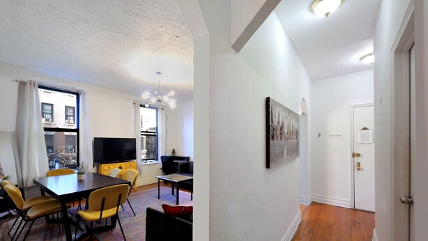 A modern living room with a dining area, a flat-screen TV, and a large window. - Midtown West Furnished 3 Bedroom Apartment (New York)