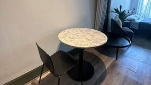 Ein kleiner Essbereich mit einem runden Tisch, zwei Stühlen, einer Zimmerpflanze und Blick auf ein Schlafzimmer mit Bett und Vorhängen.