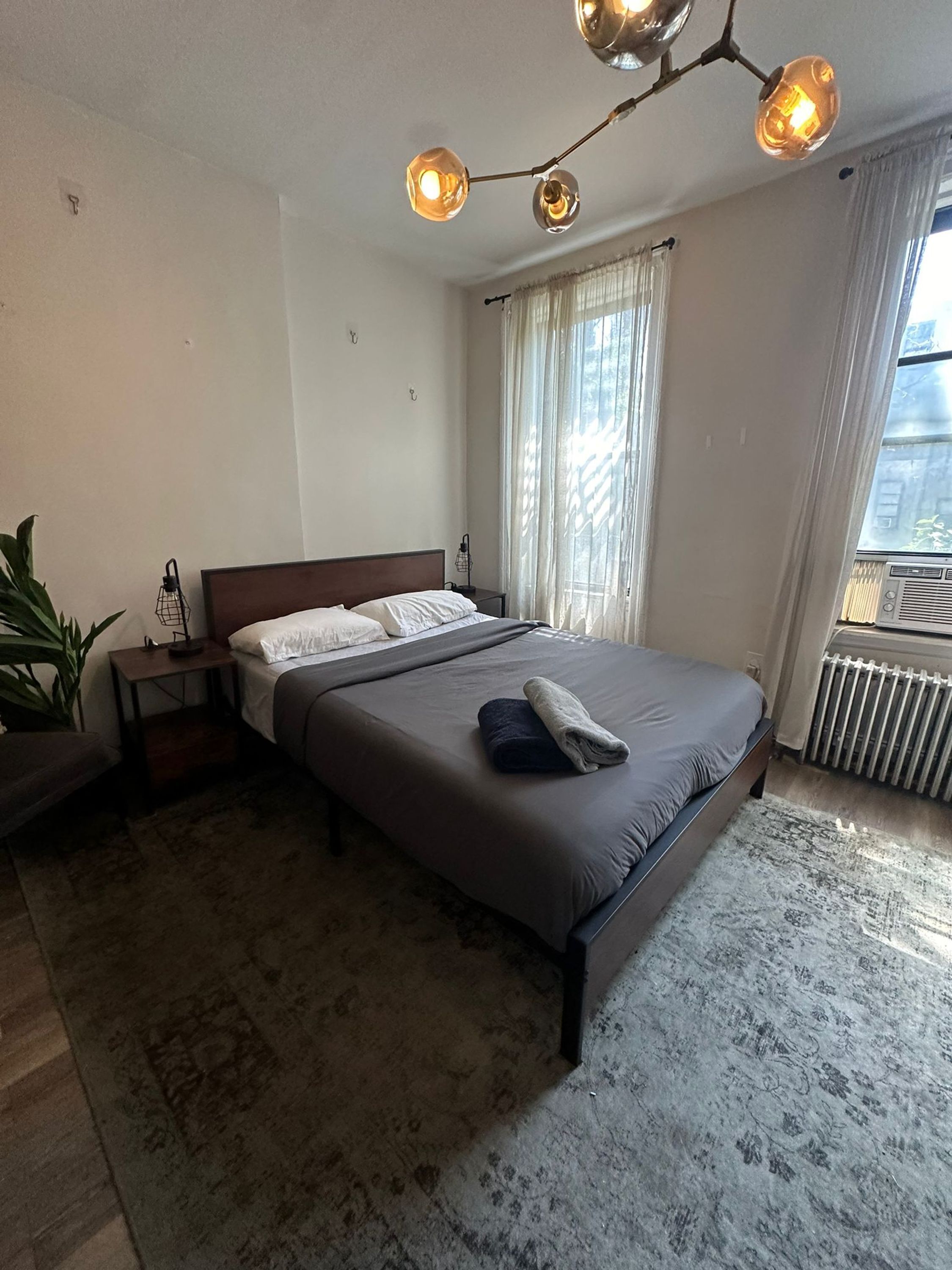 A bedroom with a bed, bedside tables, a radiator, and a window with curtains.