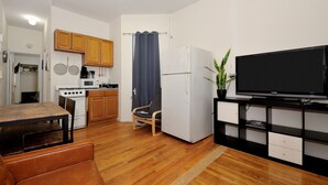 Une cuisine compacte avec des meubles en bois, une cuisinière, un four à micro-ondes et un réfrigérateur. On y trouve une table à manger avec des chaises et un téléviseur posé sur un meuble.