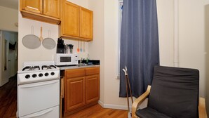 Une cuisine compacte avec des meubles en bois, une cuisinière blanche, un four à micro-ondes et un coin repas avec une chaise.