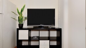 Un meuble noir pour appareils multimédias, avec un téléviseur à écran plat, une plante en pot et un livre.