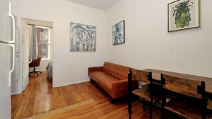Une pièce dotée d’un parquet, d’un canapé marron, d’un banc en bois et de deux tableaux abstraits accrochés aux murs.