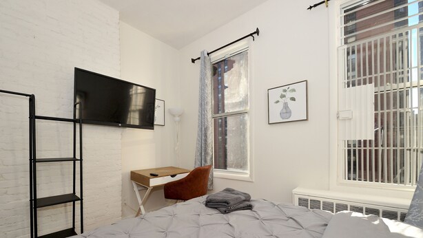 Une chambre à coucher avec un lit, un bureau, une chaise, un téléviseur et une fenêtre avec des rideaux.