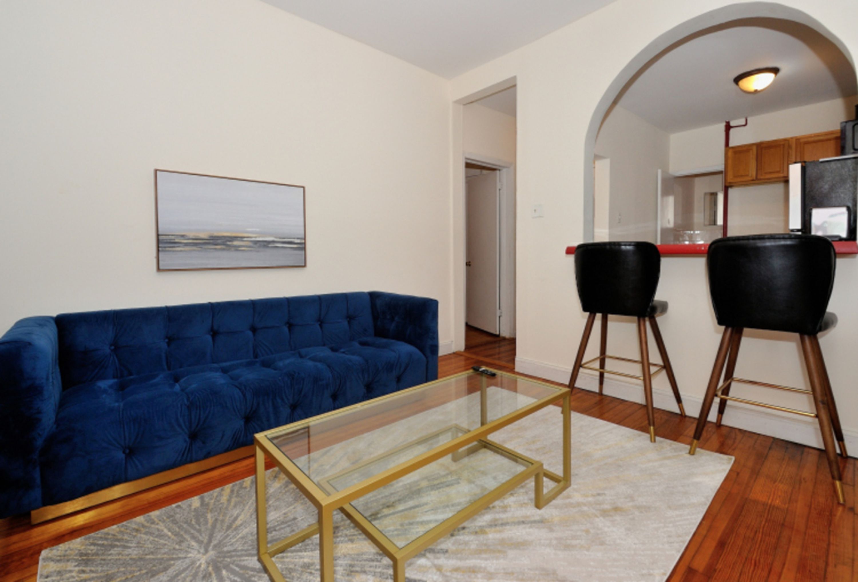A living room with a blue sofa, a glass coffee table, and two black chairs.