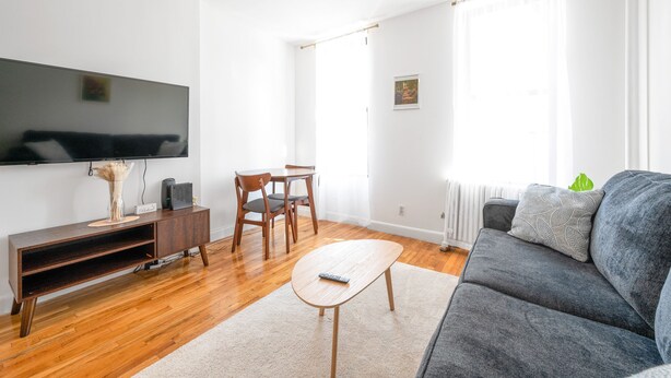 Una sala de estar con televisor de pantalla plana, muebles de madera, un sofá gris y una alfombra blanca.