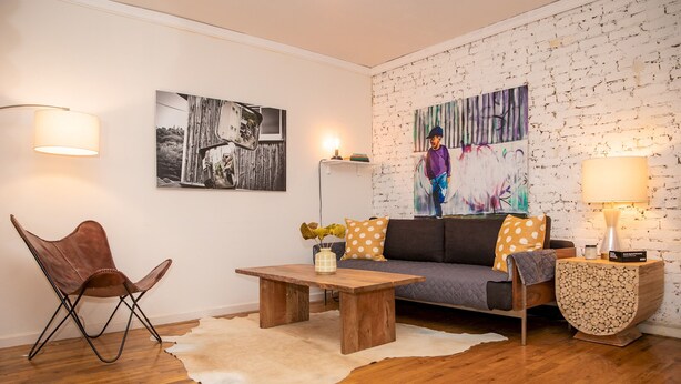 Un soggiorno con pavimento in legno, un divano con cuscini decorati, un tavolino da caffè, una poltrona in pelle e una parete con motivo decorativo e due opere d'arte.