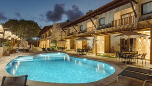 A swimming pool with lounge chairs and tables, surrounded by a building with stone walls and wooden balconies. - Maihai Porto de Galinhas (Ipojuca)