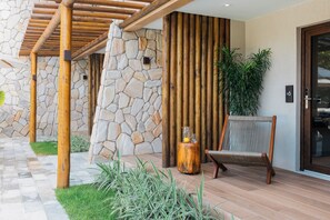 A modern outdoor area with a stone wall, wooden pergola, and a seating area with a chair and a small table. - Maihai Porto de Galinhas (Ipojuca)