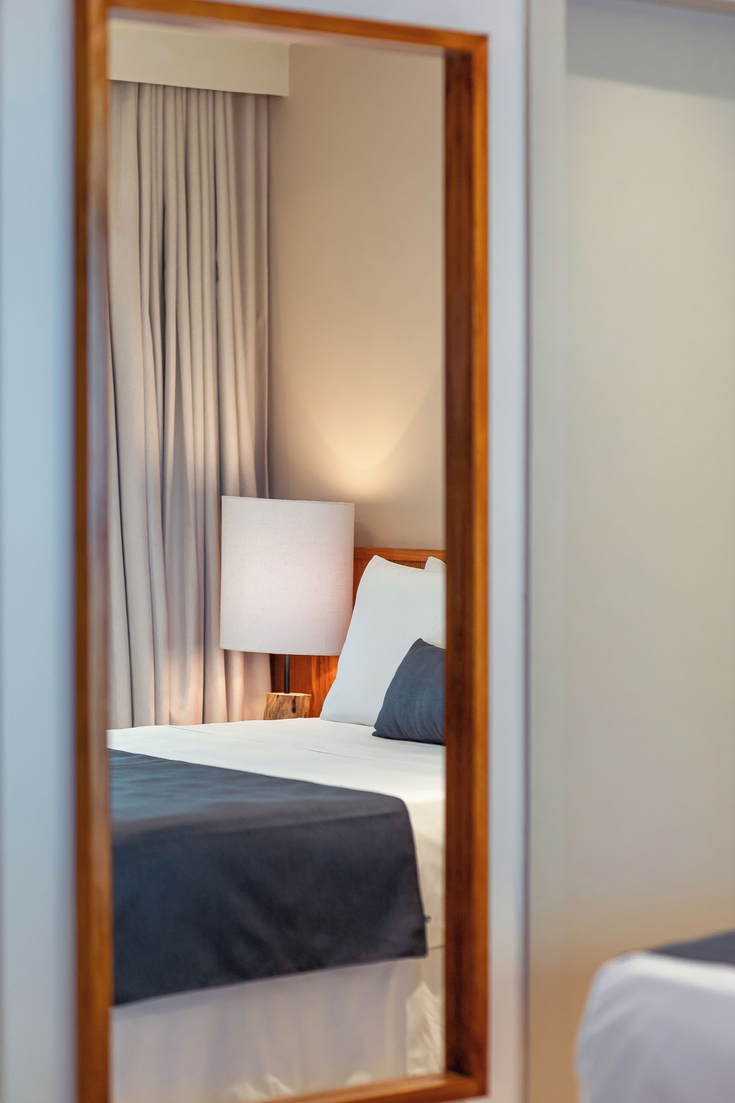 A hotel room with a bed, a nightstand, a lamp, and a view of the room through a mirror.