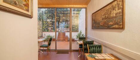 A dining area with a wooden table, green upholstered chairs, and a view of the outdoor patio through glass doors.