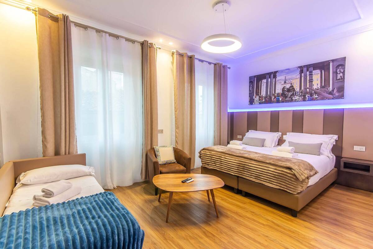 A hotel room with a bed, a sofa, a small table, and a painting on the wall.