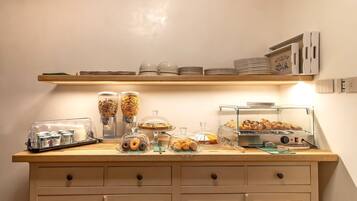Een ontbijtbuffet met diverse soorten eten en bakken, waaronder een koffieapparaat en een vitrine met gebak.